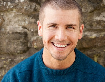 Man in blue shirt smiling in front of stone wall