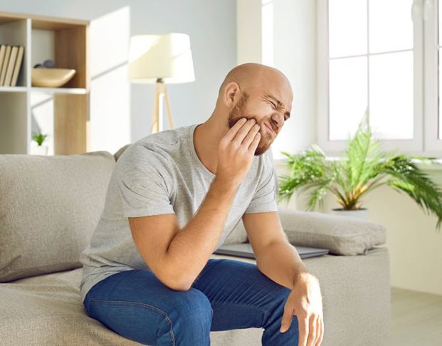 Man sitting on sofa, struggling with a toothache