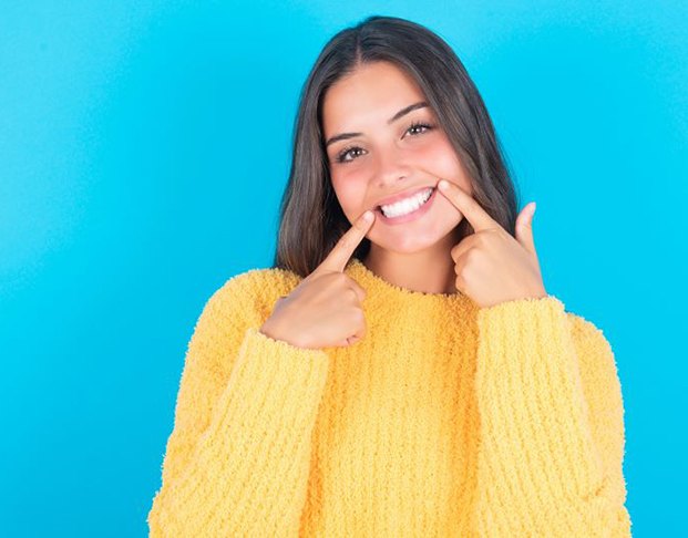 Happy woman in yellow sweater pointing at her healthy smile