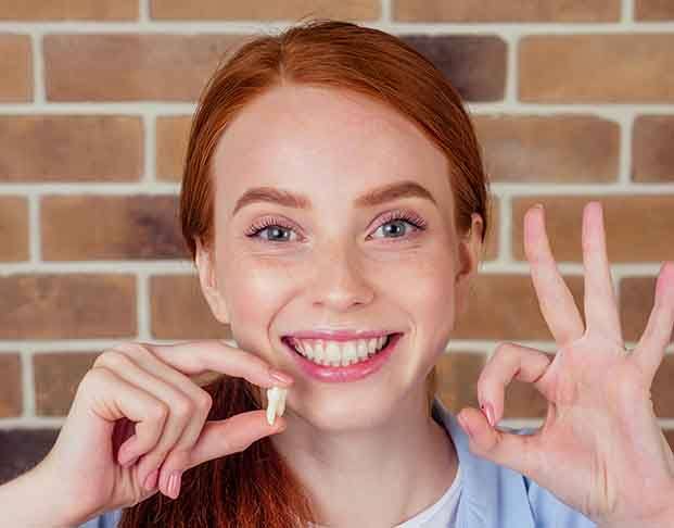 Someone holding a tooth and smiling